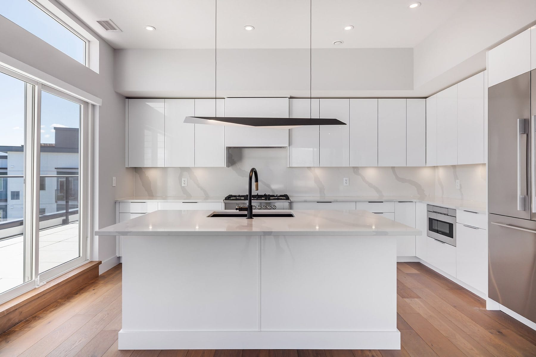 Penthouse kitchen at Green Square, Kelowna, with high gloss white cabinets, a quartz island, gas range and hardwood floors