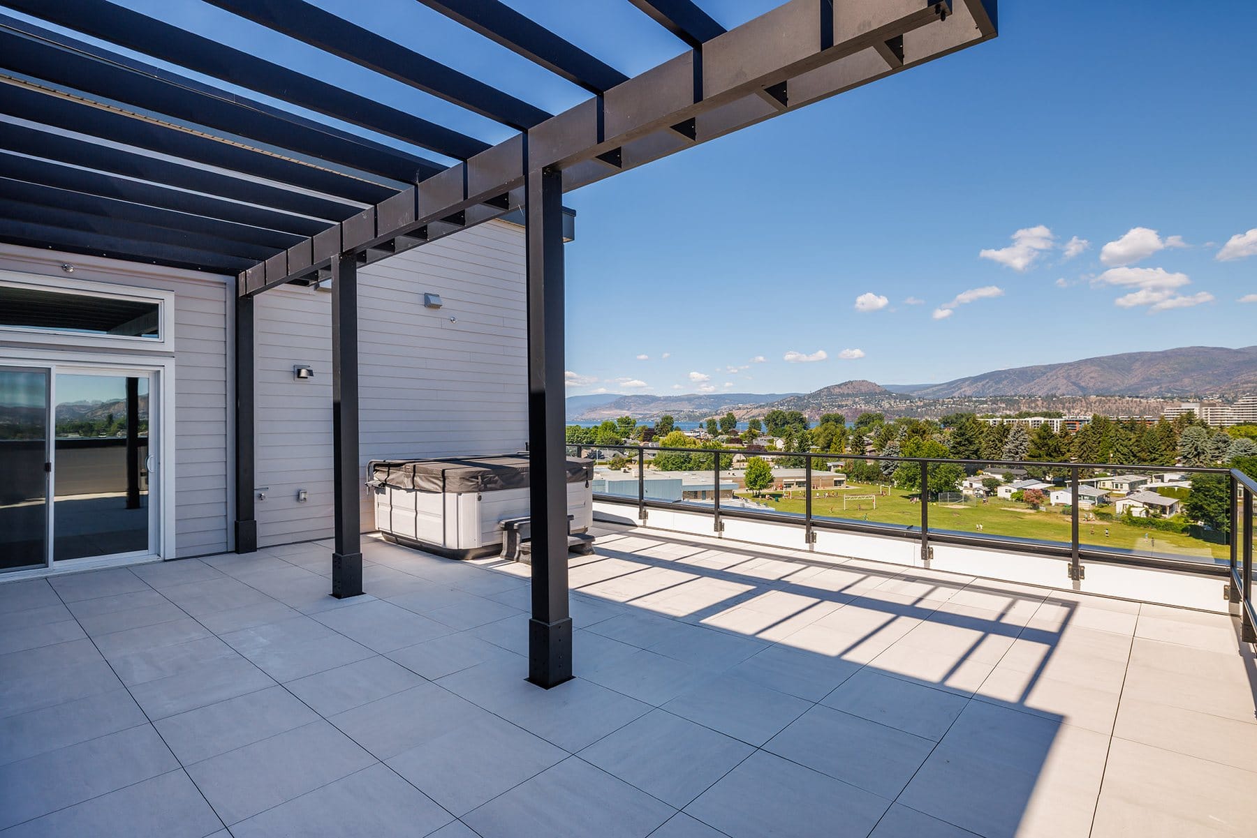 Penthouse deck at Green Square in Kelowna with the hot tub under a black pergola and mountain views
