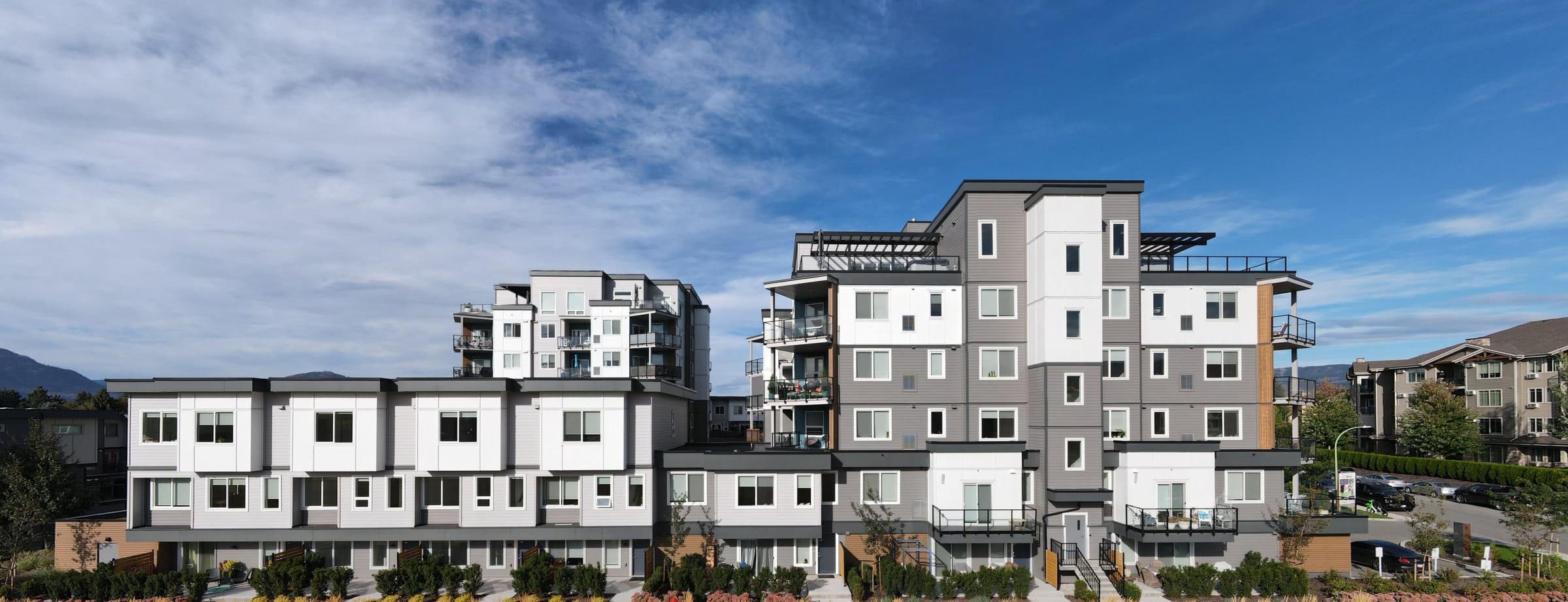 The two Vert buildings from the park: the 3642 townhome row in front with its tower behind, and 3634 with the penthouse deck on top at the right