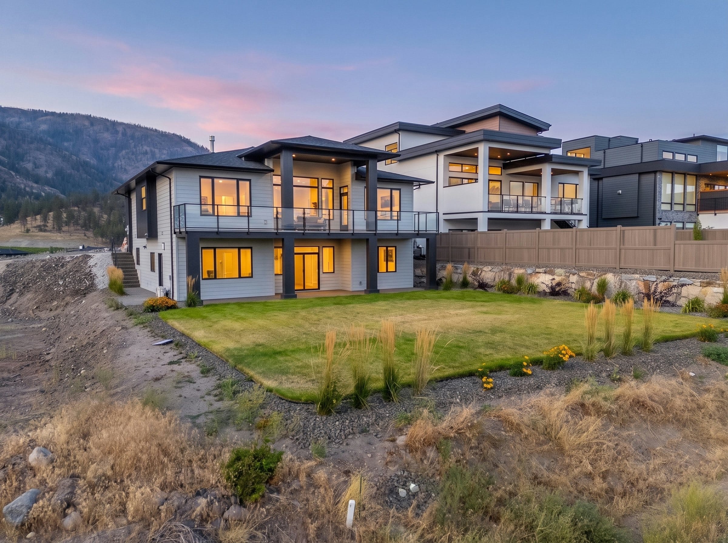 The back of the home at dusk, the deck and patio lit up over the lawn
