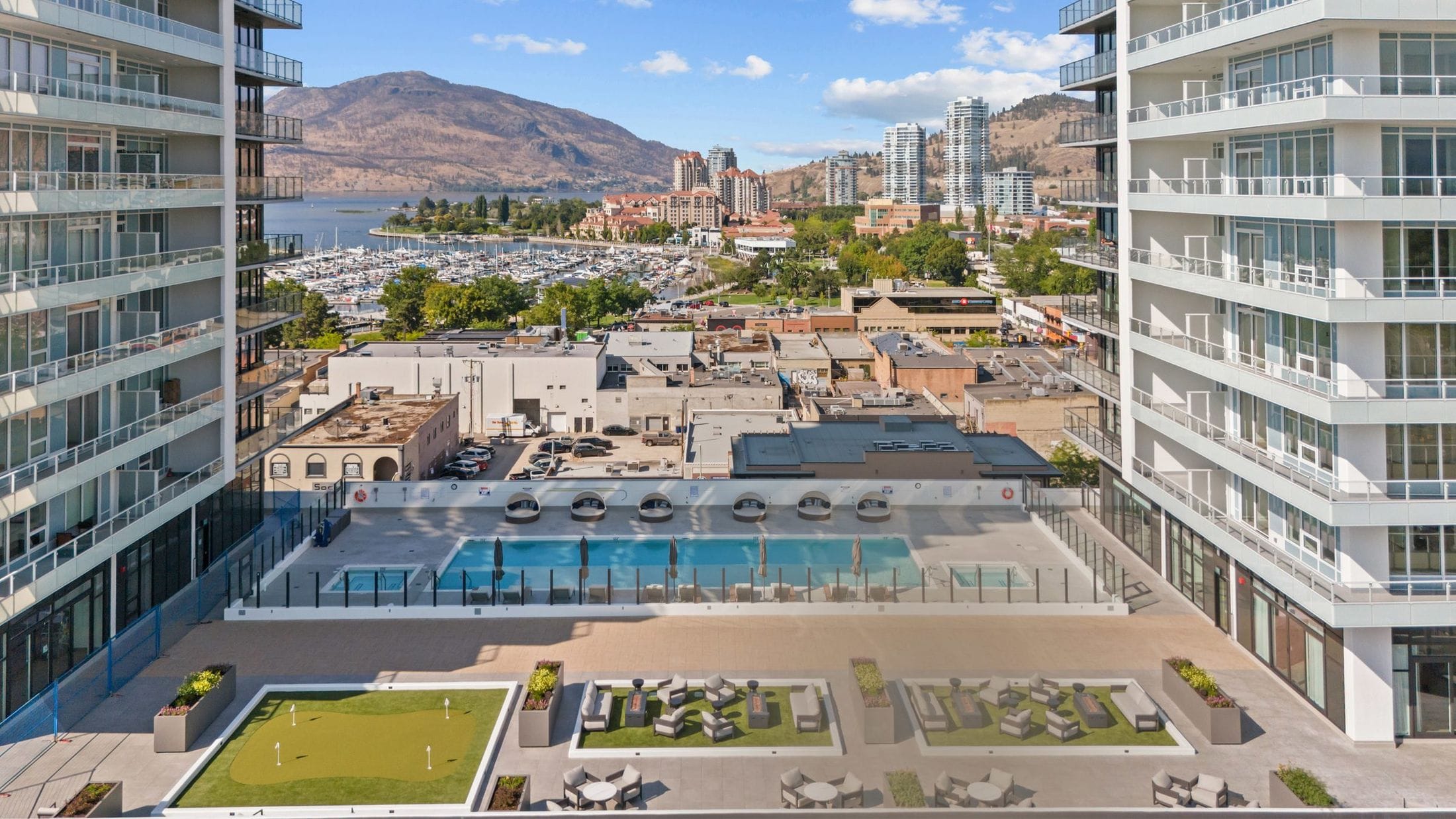 Drone frame of the pool deck between the towers, with the marina, Okanagan Lake and the mountains beyond